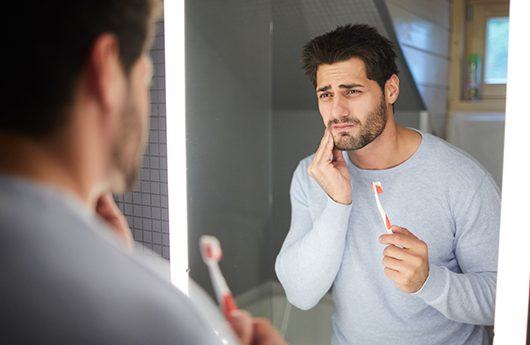 Man in pain while brushing his teeth in need of gum disease treatment