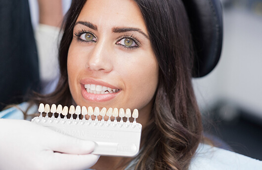 dentist holding veneers in front of woman’s face