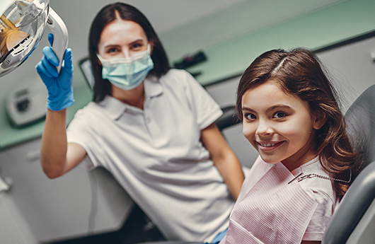 Dental team member and young girl smiling in dentistry chair