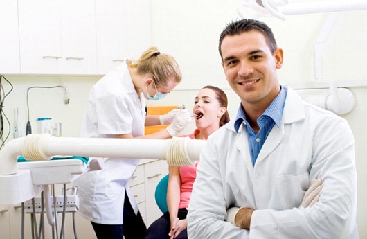 Dentist posing in front of a dentist serving a patient.