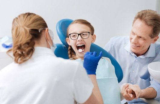 Young child examined by dentist with parent nearby.