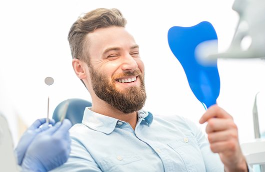 man smiling while looking in dental mirror