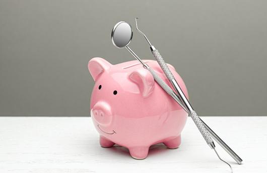 two dental instruments leaning against a pink piggy bank