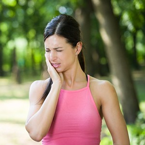 woman outdoors holding her cheek in pain 