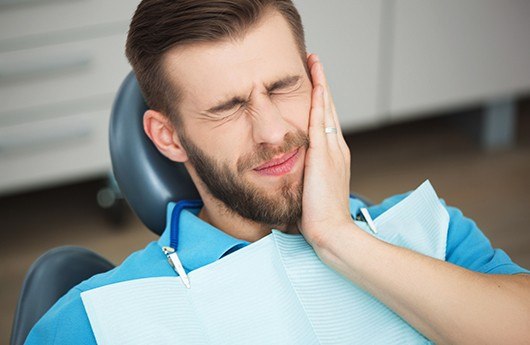 Man in pain holding cheek during emergency dental visit