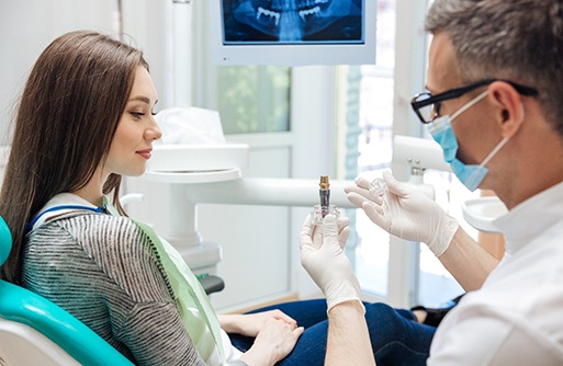 A woman looking at a dental implant model