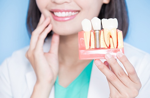 Dentist touching her jaw with one hand and holding sample dental implant in the other