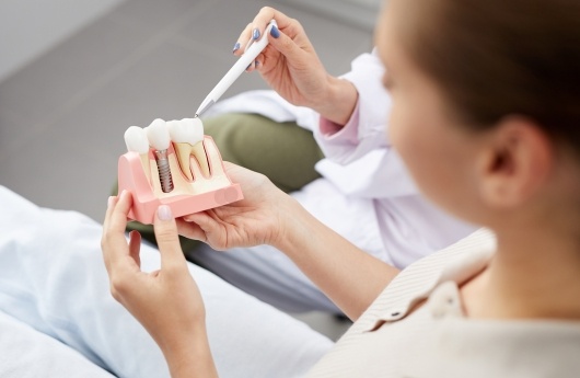 Dentist showing patient a model tooth and implant supported dental crown