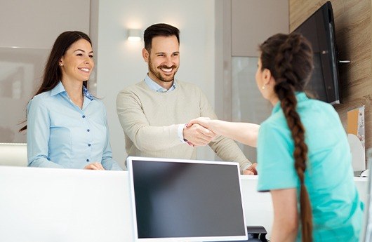 Smiling man and woman checking in at dental office reception desk