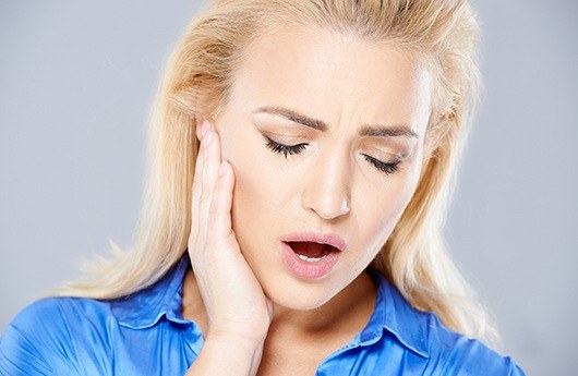 Woman in need of occlusal adjustment holding jaw