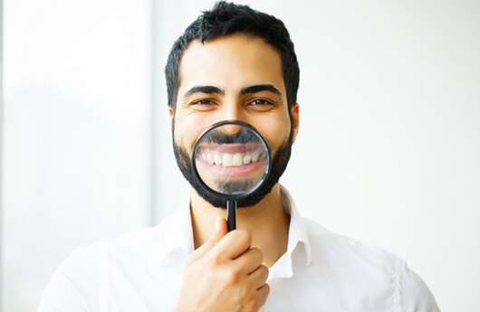 man in white dress shirt holding magnifying glass to his smile 