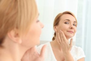 woman looking at her reflection and wondering whether she should see her emergency dentist for facial swelling