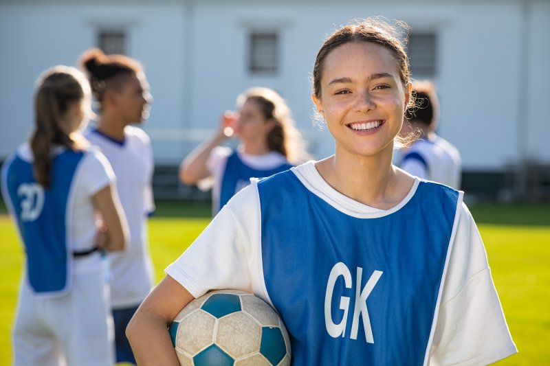 Teen with soccer ball smiling on field with teammates