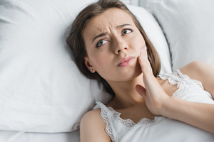 Concerned woman lying in bed with a toothache